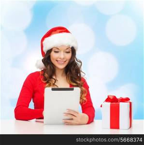 christmas, holidays, technology and people concept - smiling woman in santa helper hat with gift box and tablet pc computer over blue lights background