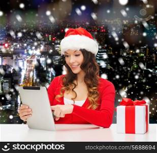christmas, holidays, technology and people concept - smiling woman in santa helper hat with gift box and tablet pc computer over snowy night city background