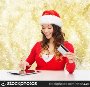 christmas, holidays, technology and shopping concept - smiling woman in santa helper hat with credit card and tablet pc computer over yellow lights background