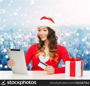 christmas, holidays, technology and shopping concept - smiling woman in santa helper hat with gift box, credit card and tablet pc computer over snowy city background
