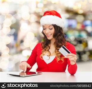 christmas, holidays, technology and shopping concept - smiling woman in santa helper hat with credit card and tablet pc computer over lights background