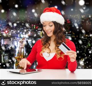 christmas, holidays, technology and shopping concept - smiling woman in santa helper hat with credit card and tablet pc computer over snowy night city background