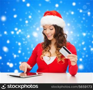 christmas, holidays, technology and shopping concept - smiling woman in santa helper hat with credit card and tablet pc computer over blue snowy background