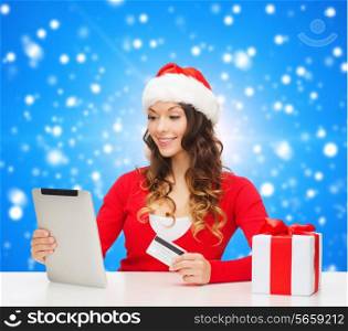 christmas, holidays, technology and shopping concept - smiling woman in santa helper hat with credit card and tablet pc computer over blue snowy background