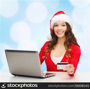 christmas, holidays, technology and shopping concept - smiling woman in santa helper hat with credit card and laptop computer over blue lights background