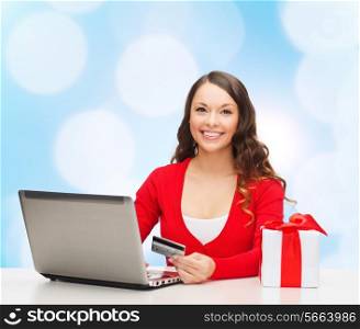 christmas, holidays, technology and shopping concept - smiling woman with credit card, gift box and laptop computer over blue lights background