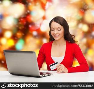 christmas, holidays, technology and shopping concept - smiling woman with credit card and laptop computer over red lights background
