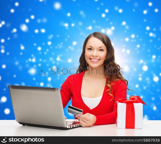 christmas, holidays, technology and shopping concept - smiling woman with credit card, gift box and laptop computer over blue snowing background