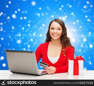 christmas, holidays, technology and shopping concept - smiling woman with credit card, gift box and laptop computer over blue snowing background