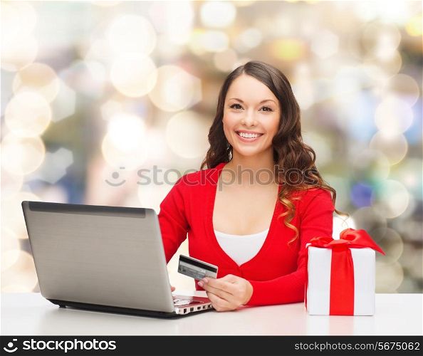 christmas, holidays, technology and shopping concept - smiling woman with credit card, gift box and laptop computer over lights background