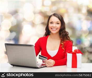 christmas, holidays, technology and shopping concept - smiling woman with credit card, gift box and laptop computer over lights background