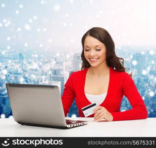christmas, holidays, technology and shopping concept - smiling woman with credit card and laptop computer over snowy city background