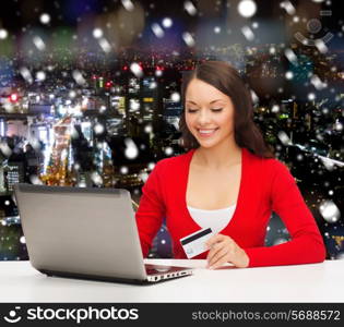 christmas, holidays, technology and shopping concept - smiling woman with credit card and laptop computer over snowy night city background