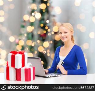 christmas, holidays, technology and shopping concept - smiling woman with gift boxes, credit card and laptop computer over christmas tree background
