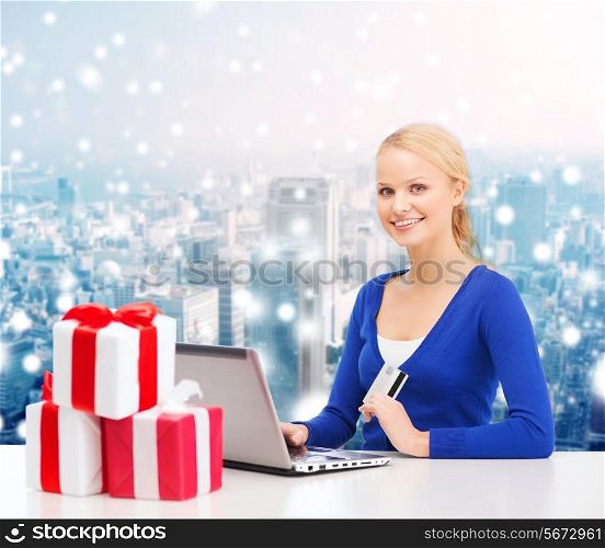 christmas, holidays, technology and shopping concept - smiling woman with gift boxes, credit card and laptop computer over snowy city background