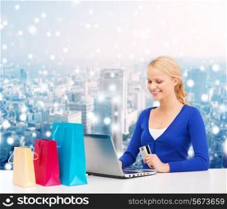 christmas, holidays, technology and shopping concept - smiling woman with shopping bags, credit card and laptop computer over snowy city background