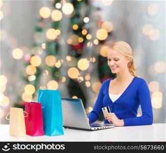 christmas, holidays, technology and shopping concept - smiling woman with shopping bags, credit card and laptop computer over christmas tree background