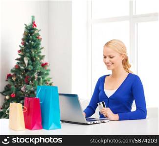 christmas, holidays, technology and shopping concept - smiling woman with shopping bags, credit card and laptop computer over living room with christmas tree background