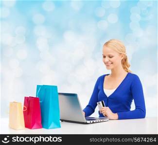christmas, holidays, technology and shopping concept - smiling woman with shopping bags, credit card and laptop computer over blue lights background