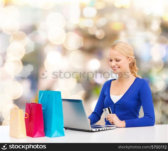christmas, holidays, technology and shopping concept - smiling woman with shopping bags, credit card and laptop computer over lights background