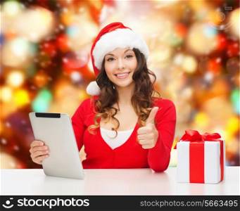 christmas, holidays, technology, gesture and people concept - smiling woman in santa helper hat with gift box and tablet pc computer showing thumbs up over red lights background