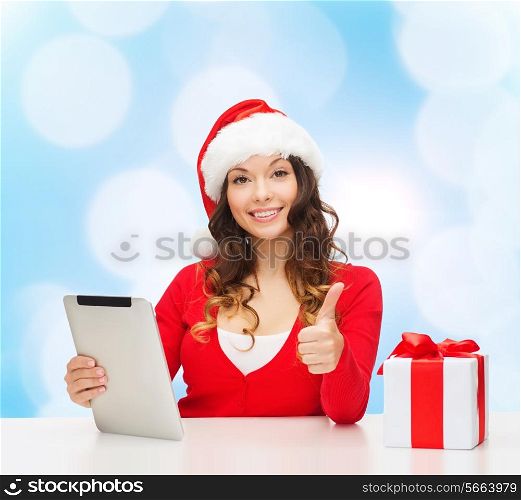 christmas, holidays, technology, gesture and people concept - smiling woman in santa helper hat with gift box and tablet pc computer showing thumbs up over blue lights background