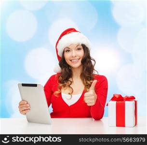christmas, holidays, technology, gesture and people concept - smiling woman in santa helper hat with gift box and tablet pc computer showing thumbs up over blue lights background