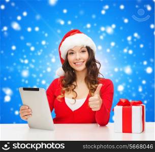 christmas, holidays, technology, gesture and people concept - smiling woman in santa helper hat with gift box and tablet pc computer showing thumbs up over blue snowy background