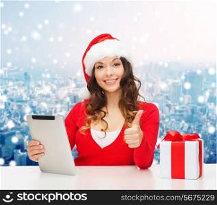 christmas, holidays, technology, gesture and people concept - smiling woman in santa helper hat with gift box and tablet pc computer showing thumbs up over snowy city background