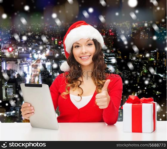 christmas, holidays, technology, gesture and people concept - smiling woman in santa helper hat with gift box and tablet pc computer showing thumbs up over snowy night city background