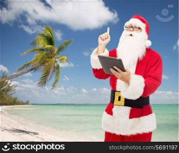 christmas, holidays, technology, travel and people concept - man in costume of santa claus with tablet pc computer pointing finger up over tropical beach background
