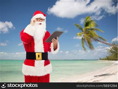 christmas, holidays, technology, travel and people concept - man in costume of santa claus with tablet pc computer over tropical beach background