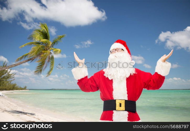 christmas, holidays, travel and people concept - man in costume of santa claus with raised hands over tropical beach background