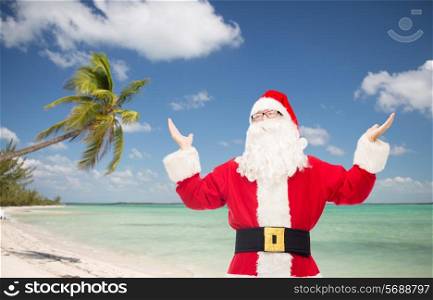 christmas, holidays, travel and people concept - man in costume of santa claus with raised hands over tropical beach background
