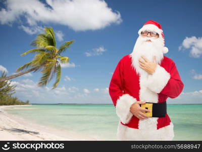 christmas, holidays, travel and people concept - man in costume of santa claus over tropical beach background