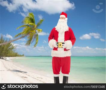 christmas, holidays, travel and people concept - man in costume of santa claus over tropical beach background over tropical beach background