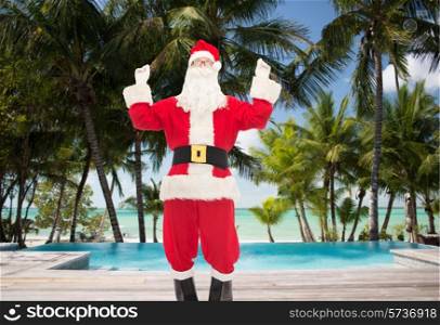 christmas, holidays, travel and people concept - man in costume of santa claus having fun over swimming pool on tropical beach background