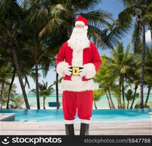 christmas, holidays, travel and people concept - man in costume of santa claus over swimming pool on tropical beach background