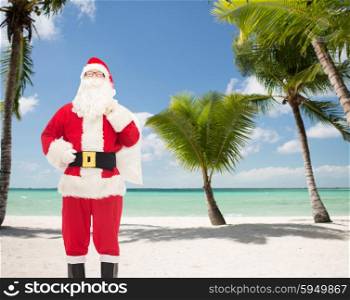 christmas, holidays, travel and people concept - man in costume of santa claus with bag over tropical beach background