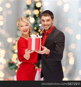 christmas, holidays, valentine&#39;s day, celebration and people concept - smiling man and woman with present over living room and christmas tree background