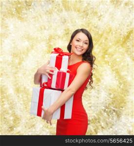 christmas, holidays, valentine&#39;s day, celebration and people concept - smiling woman in red dress with gift boxes over yellow lights background
