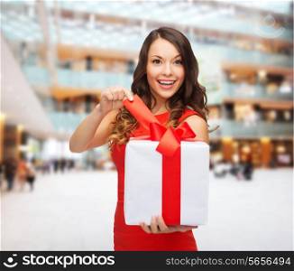 christmas, holidays, valentine&#39;s day, celebration and people concept - smiling woman in red dress with gift box over shopping center background