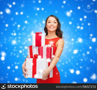 christmas, holidays, valentine&#39;s day, celebration and people concept - smiling woman in red dress with gift boxes over blue snowy background