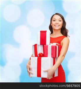 christmas, holidays, valentine&#39;s day, celebration and people concept - smiling woman in red dress with gift boxes over blue lights background