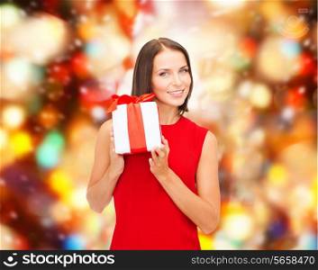 christmas, holidays, valentine&#39;s day, celebration and people concept - smiling woman in red dress with gift box over redlights background