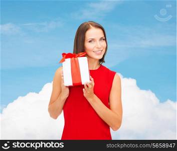 christmas, holidays, valentine&#39;s day, celebration and people concept - smiling woman in red dress with gift box over blue sky and white cloud background