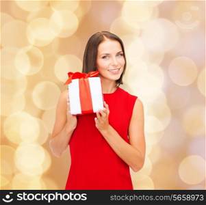 christmas, holidays, valentine&#39;s day, celebration and people concept - smiling woman in red dress with gift box over beige lights background