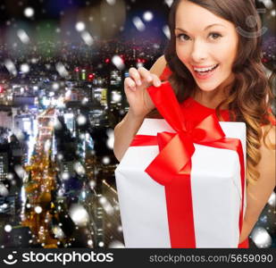 christmas, holidays, valentine&#39;s day, celebration and people concept - smiling woman in red dress with gift box over snowy night city background