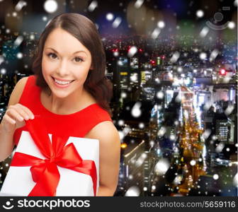 christmas, holidays, valentine&#39;s day, celebration and people concept - smiling woman in red dress with gift box over snowy night city background