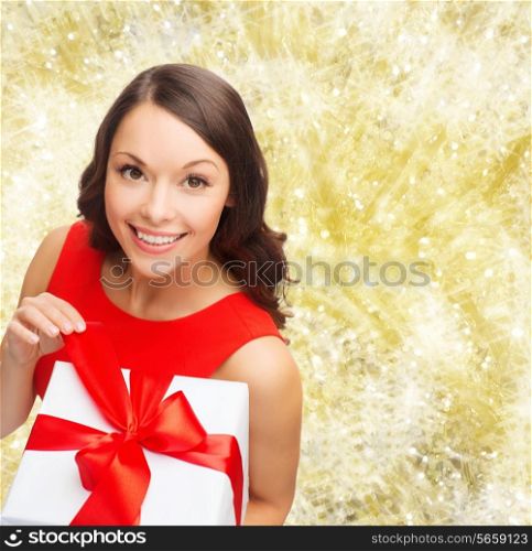 christmas, holidays, valentine&#39;s day, celebration and people concept - smiling woman in red dress with gift box over yellow lights background